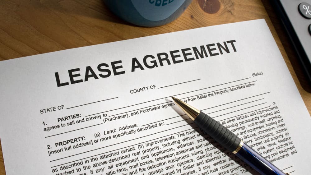 A lease agreement form with a pen on a wooden table, partially visible, with a blue mug in the background.